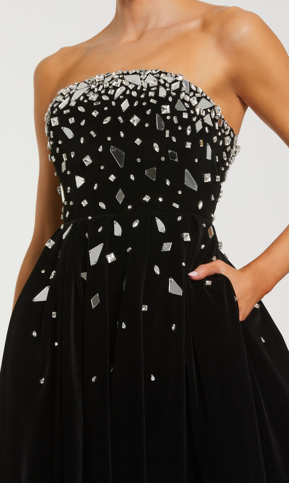 A person in the Mac Duggal 56197 long formal dress—strapless black velvet with a rhinestone and silver stud-embellished bodice—rests a hand in the side pocket.
